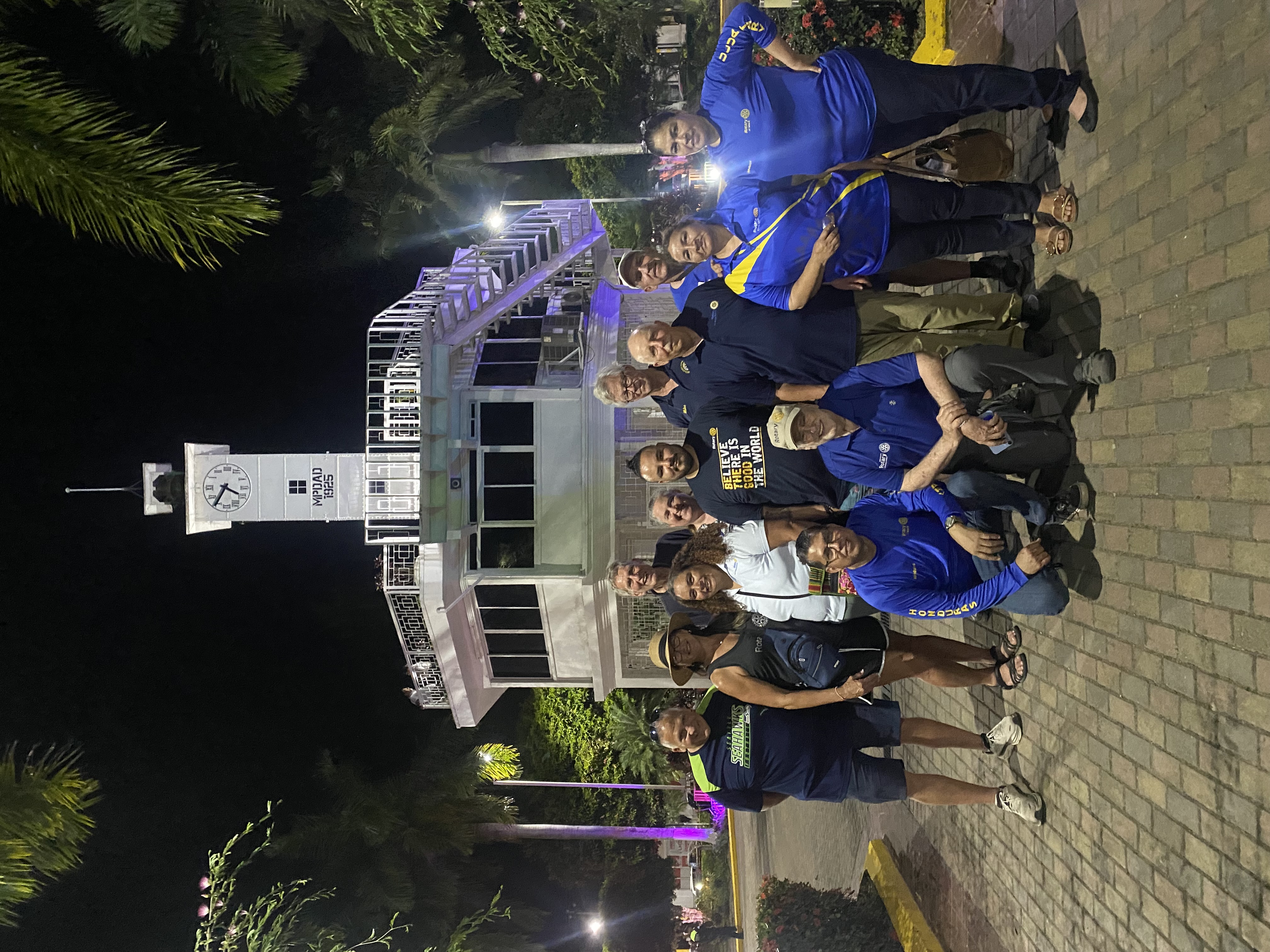 Rotarians gathered at night by a lit clock tower in Honduras.